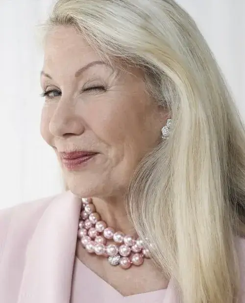 An elderly woman with long, healthy blonde hair smiling and winking, showcasing the benefits of TruVarin Hair Growth Supplement.